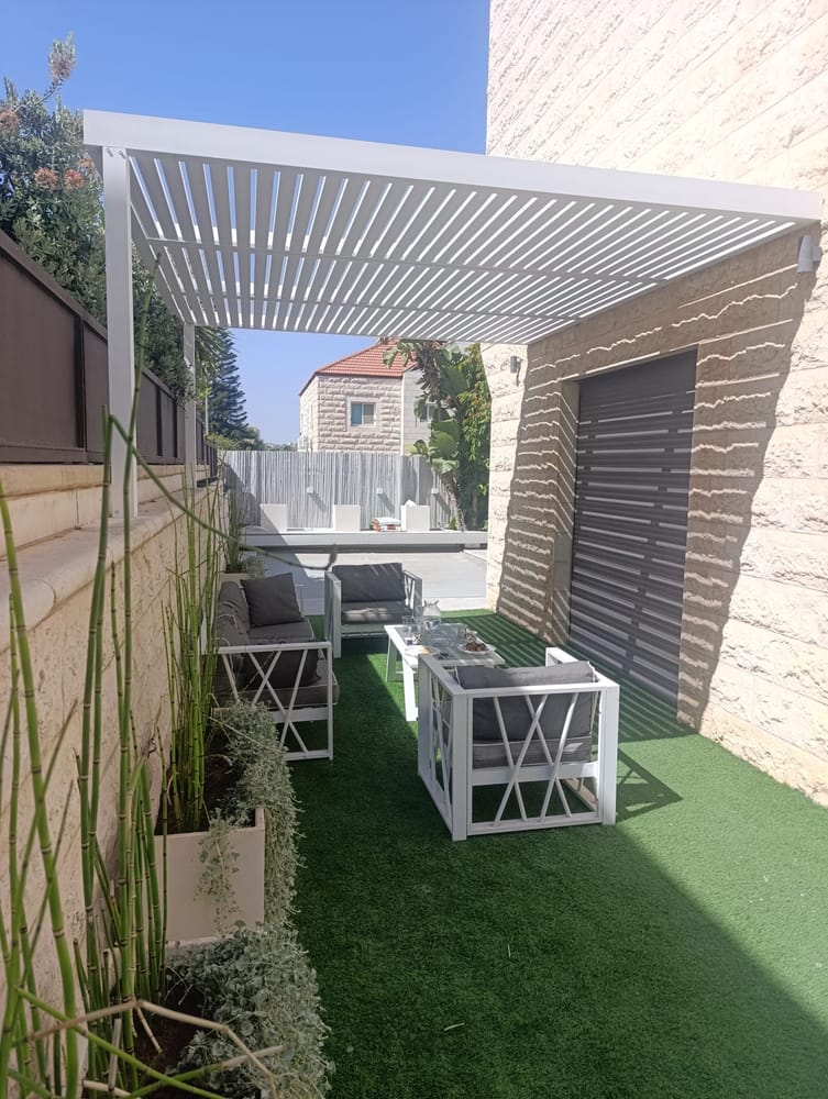 פרגולת אלומיניום לבנה מעל פינת ישיבה מוצלת עם דשא סינטטי